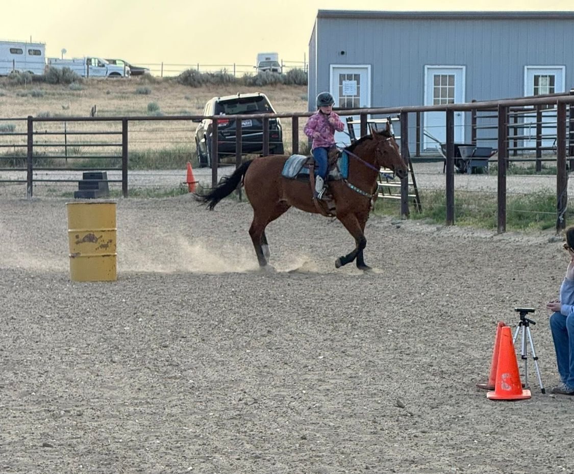 Young rider running a barrel pattern in the outdoor arena