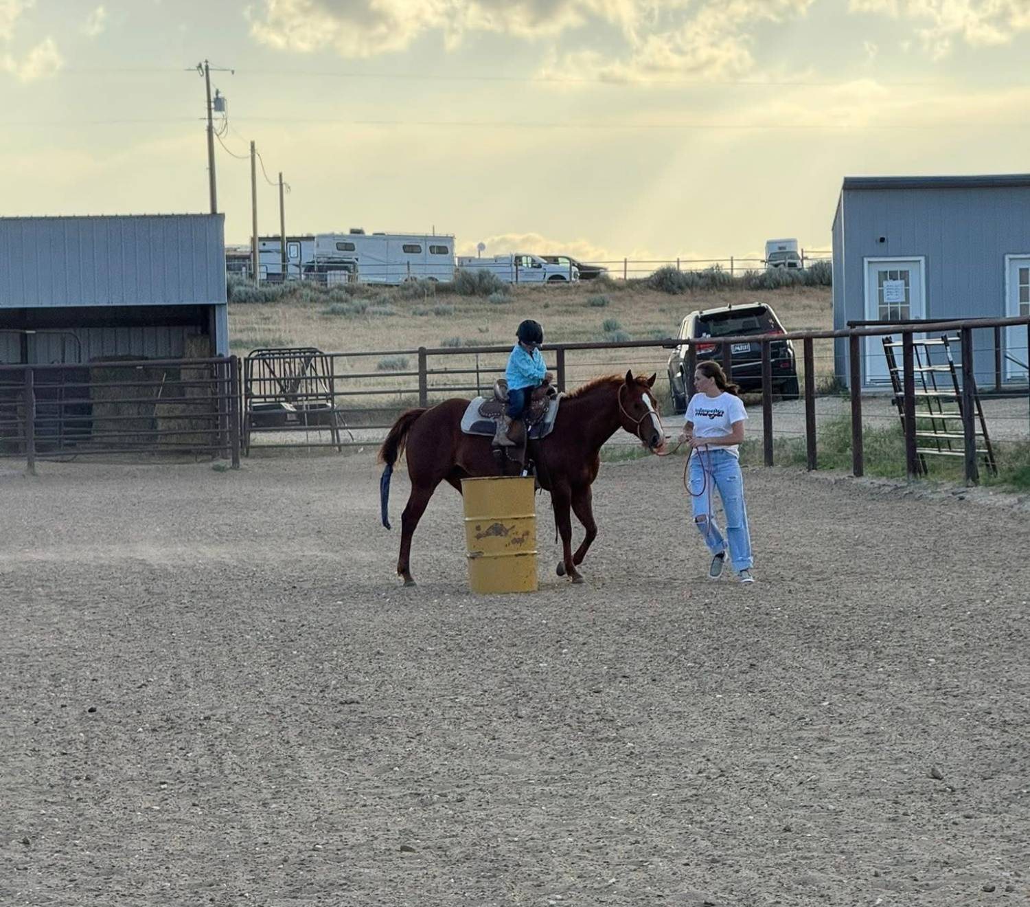 Young rider on a lesson horse rounding a barrel with an instructor walking alongside